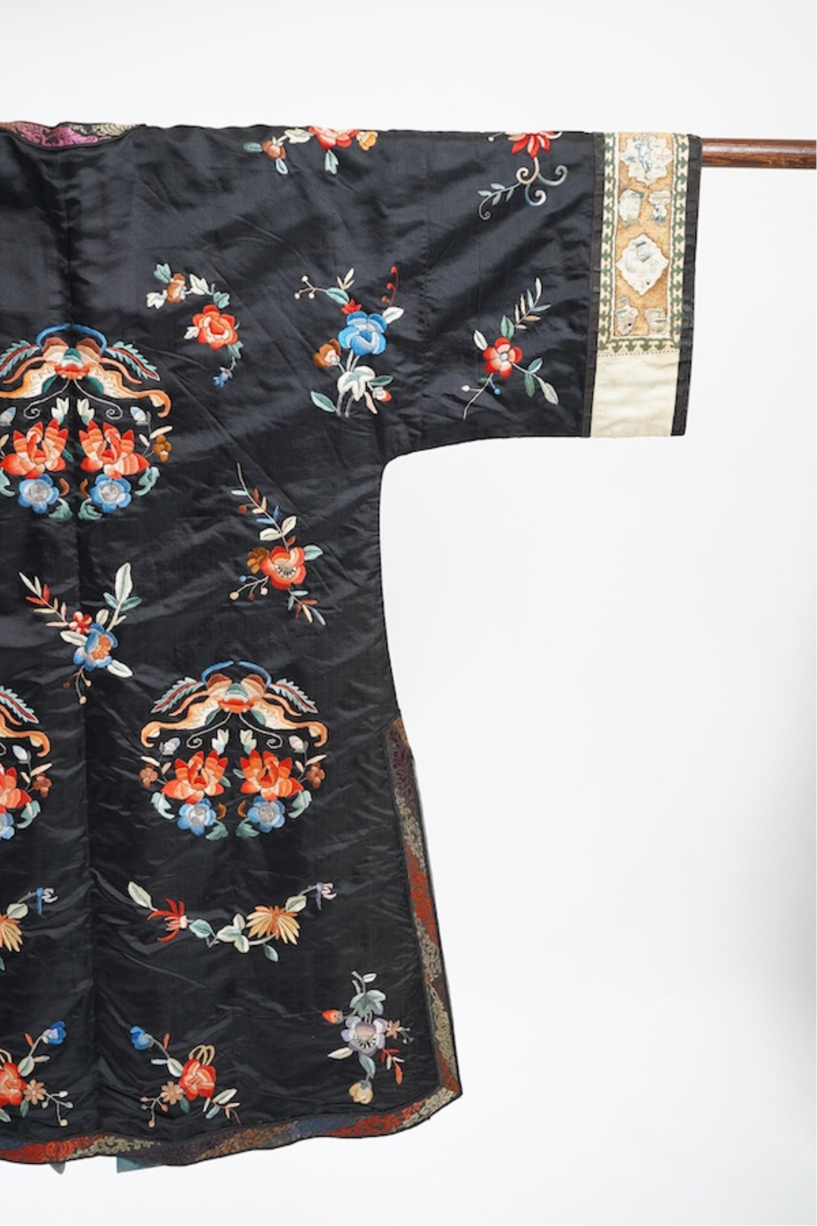 A late 19th early 20th century Chinese black silk polychrome embroidered ladies robe, decorated with cream silk, gilt and Peking knot bordered sleeve bands. The sleeve bands worked with fine figural and other embroidered